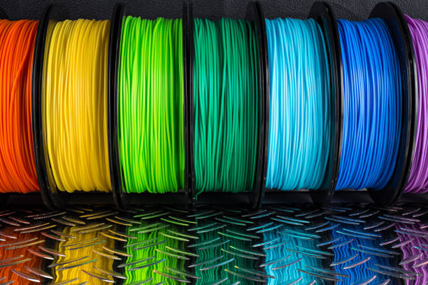 colorful bright row of spool 3d printer pla abs filament plastic material on dark black metal steel diamond plate background